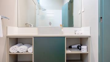 Een moderne badkamer met een grote spiegel, een wastafel en planken met handdoeken en toiletartikelen.