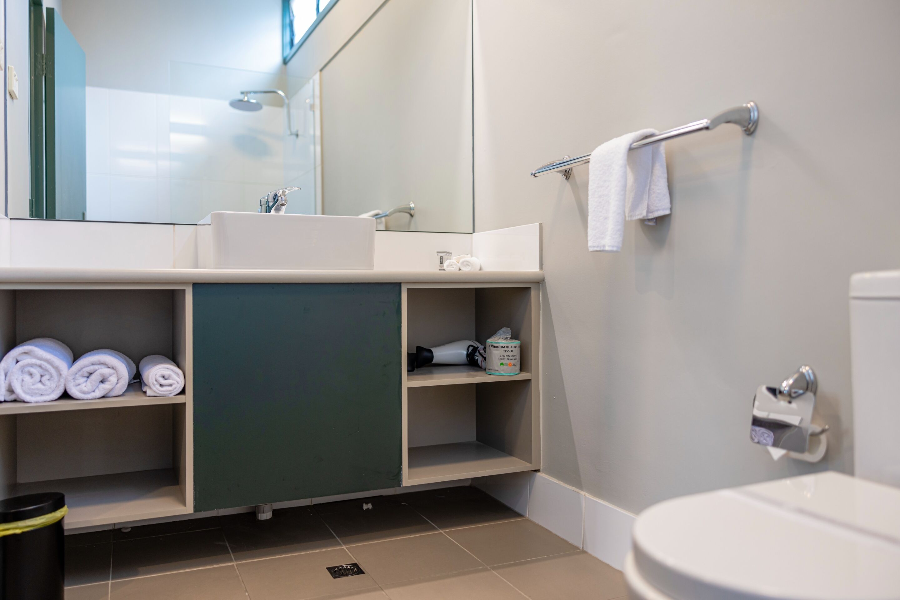 Un baño moderno con lavamanos, espejo, toallero y retrete.