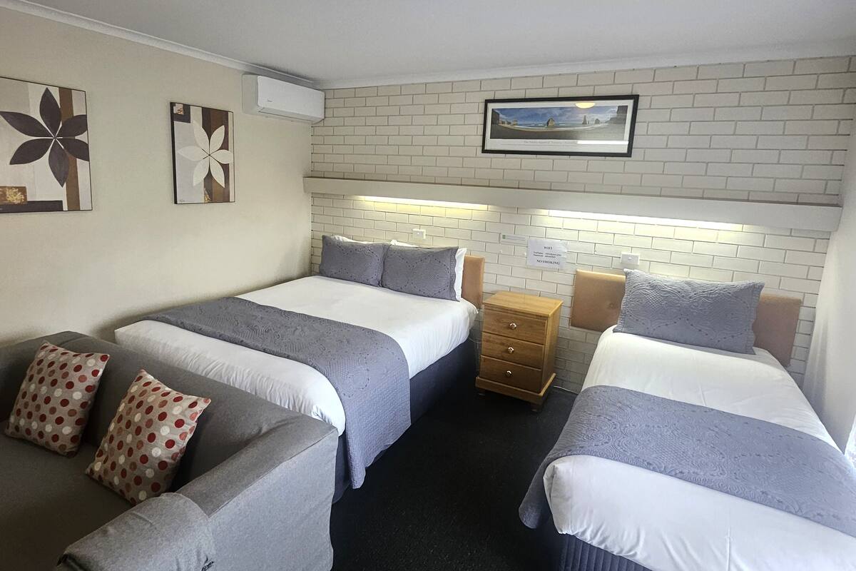 A hotel room with two beds, a small wooden nightstand, and a wall-mounted air conditioner.