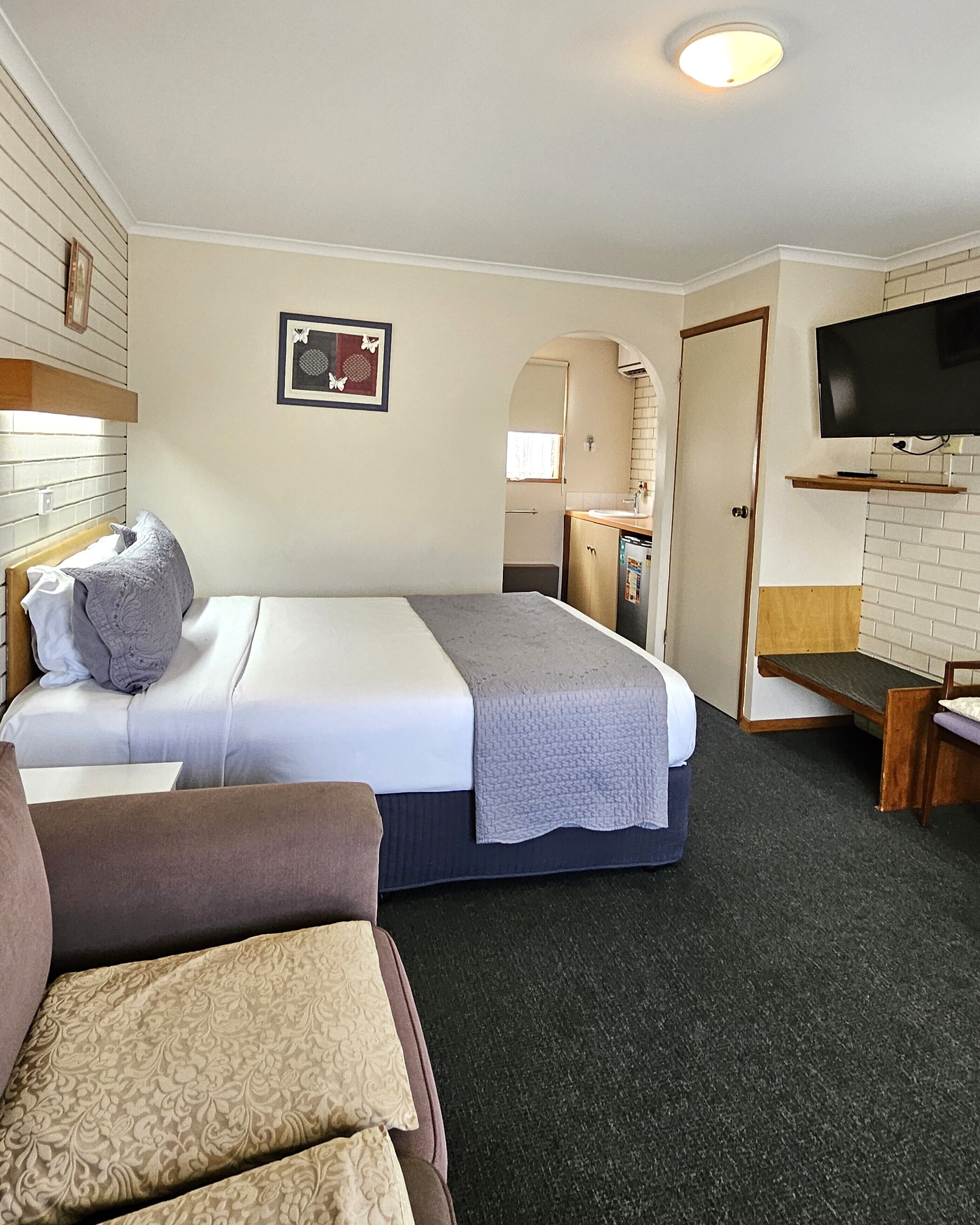 A hotel room with a bed, a sofa, a television, and a small kitchenette.
