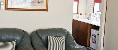 Une pièce comprenant un canapé, un lit, un tableau encadré et un coin cuisine visible à travers une arche.