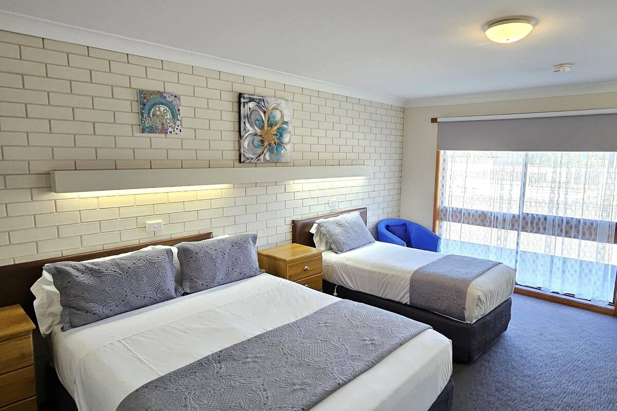 A hotel room with two beds, a brick-patterned wall, and artwork.