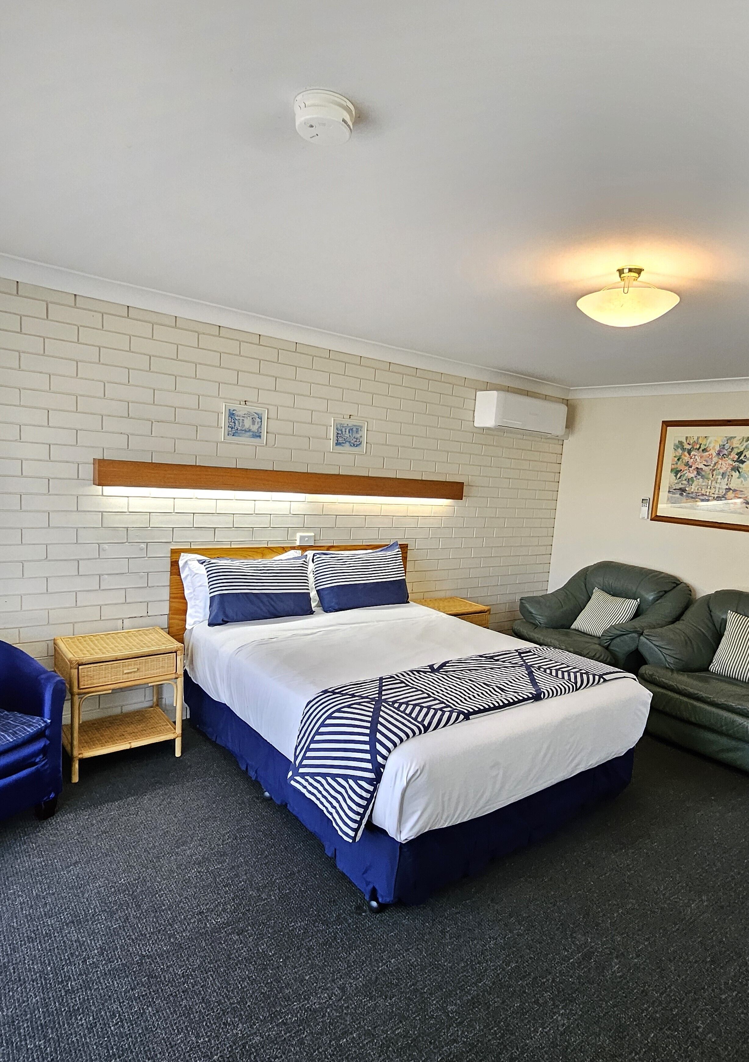 Une chambre d’hôtel avec un lit, un canapé vert, une petite table et un climatiseur fixé au mur.