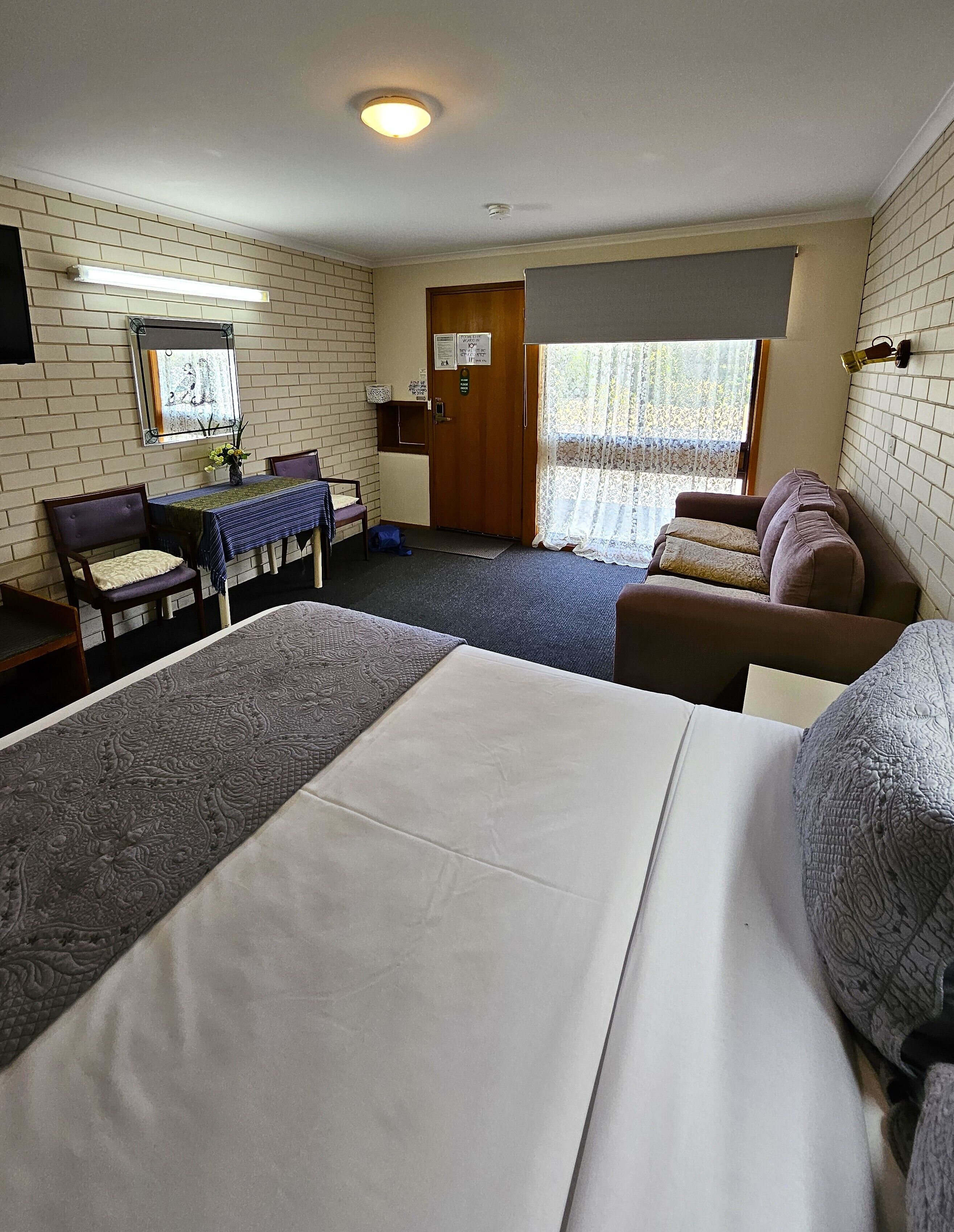 Una habitación de hotel con una cama grande, un sofá, una mesa de comedor con sillas, una pequeña cocina y una ventana con cortinas.