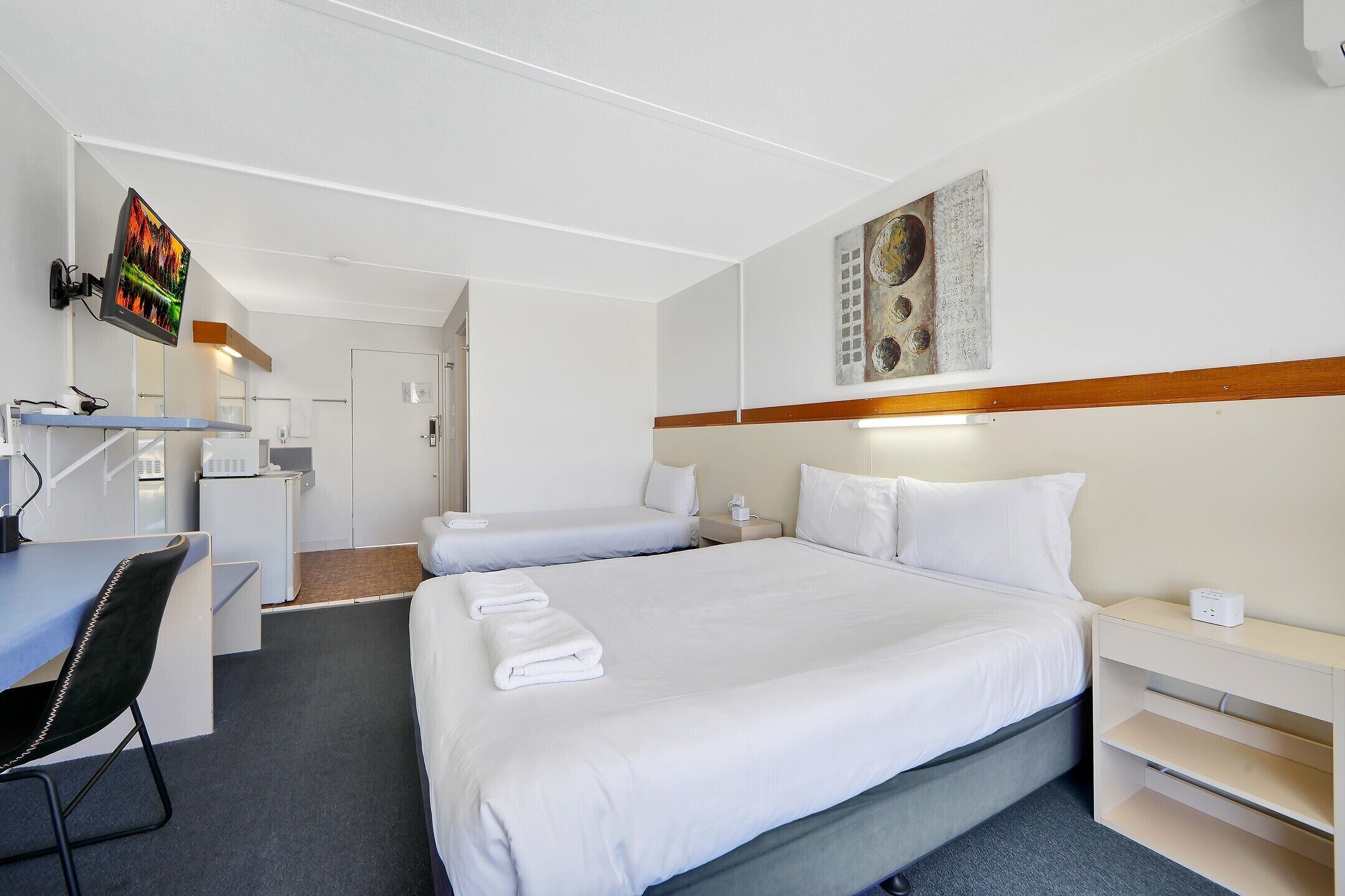 Ein Hotelzimmer mit einem großen Bett, einem Schreibtisch, einem Sessel, einem Fernseher und einem Bild an der Wand.