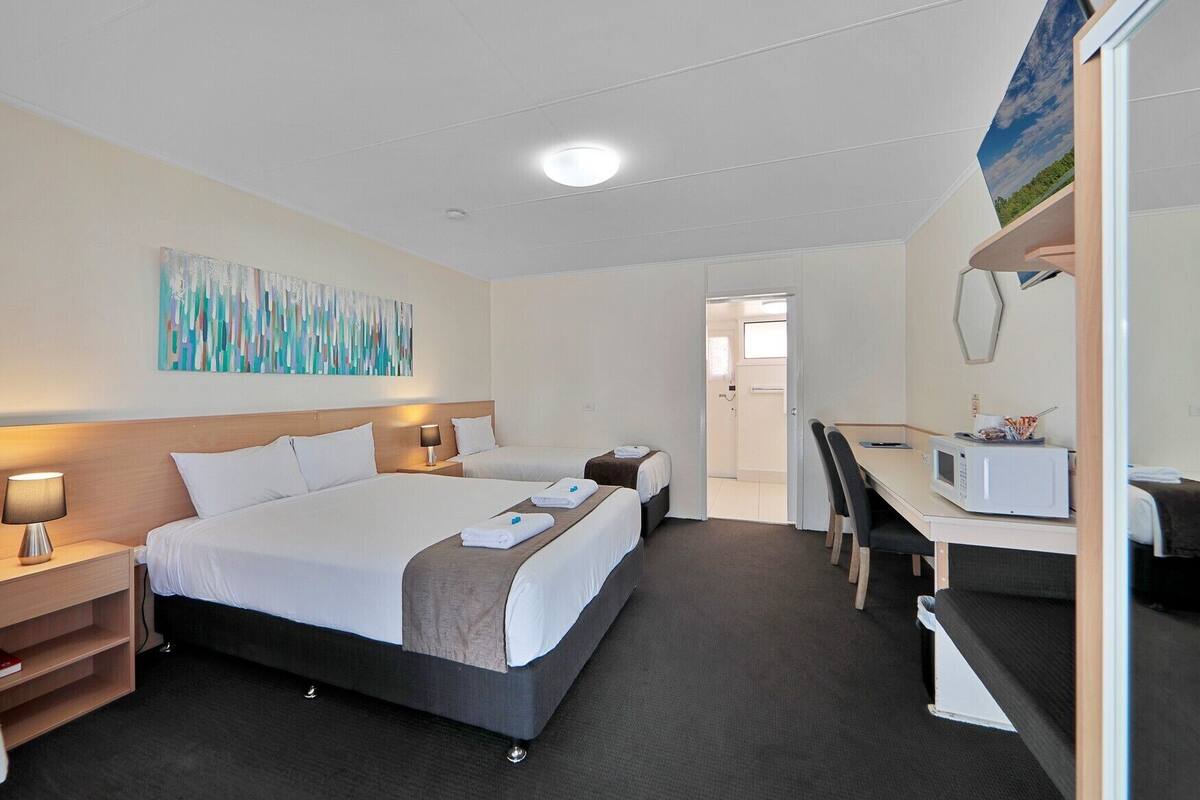 A hotel room with two beds, a desk, a microwave, and a painting on the wall.