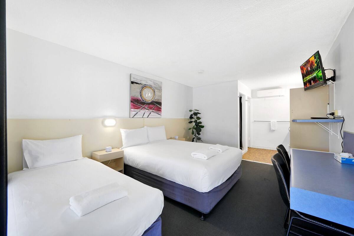 A hotel room with two beds, a desk, a chair, a TV, and a painting on the wall.