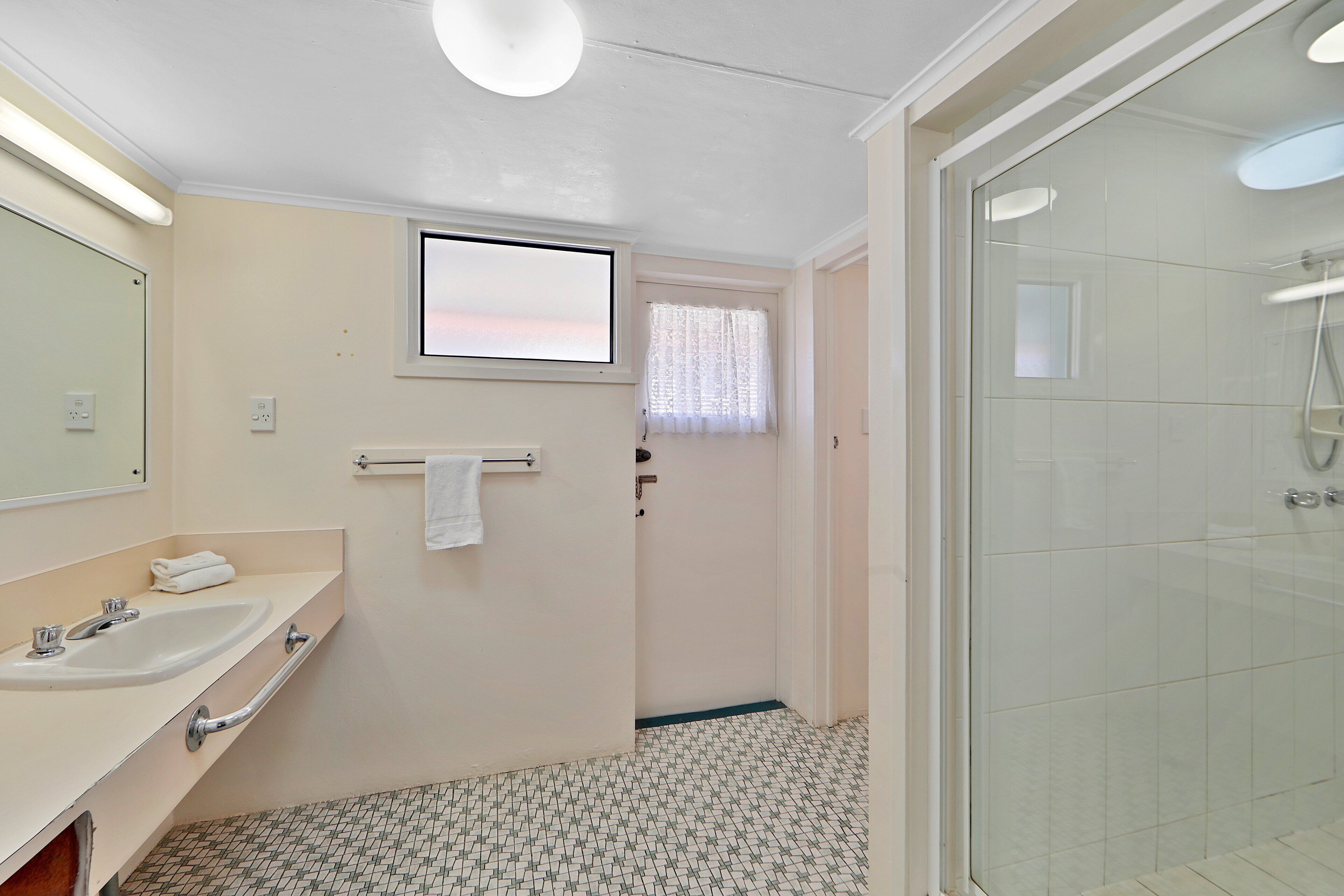 A bathroom with a sink, mirror, and shower.