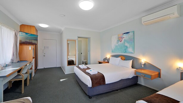A hotel room with a bed, bedside table, lamp, desk, chair, and a bathroom door. - Oscar Motel (Bundaberg West)