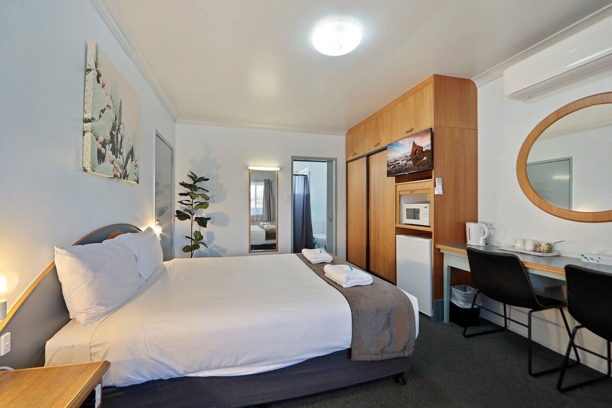 A hotel room with a bed, desk, chair, and a mirror.