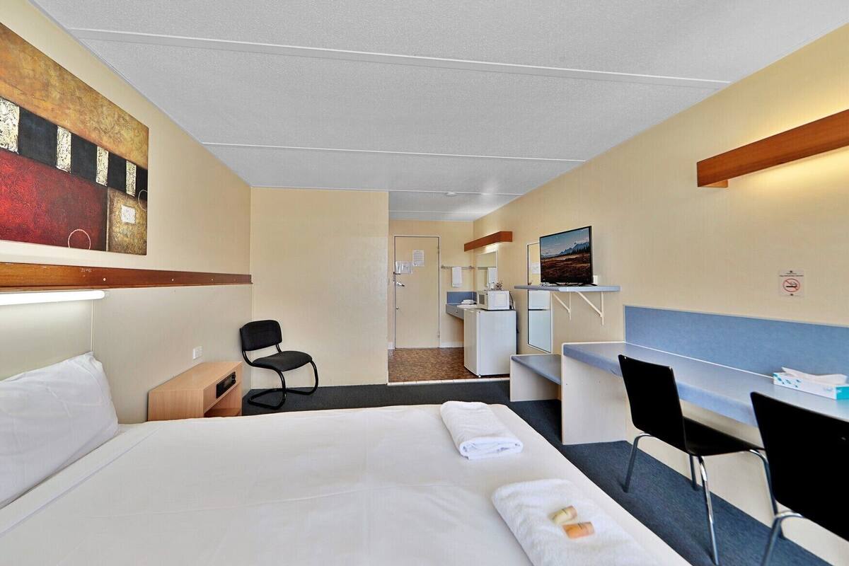 A hotel room with a bed, desk, chair, and a television.