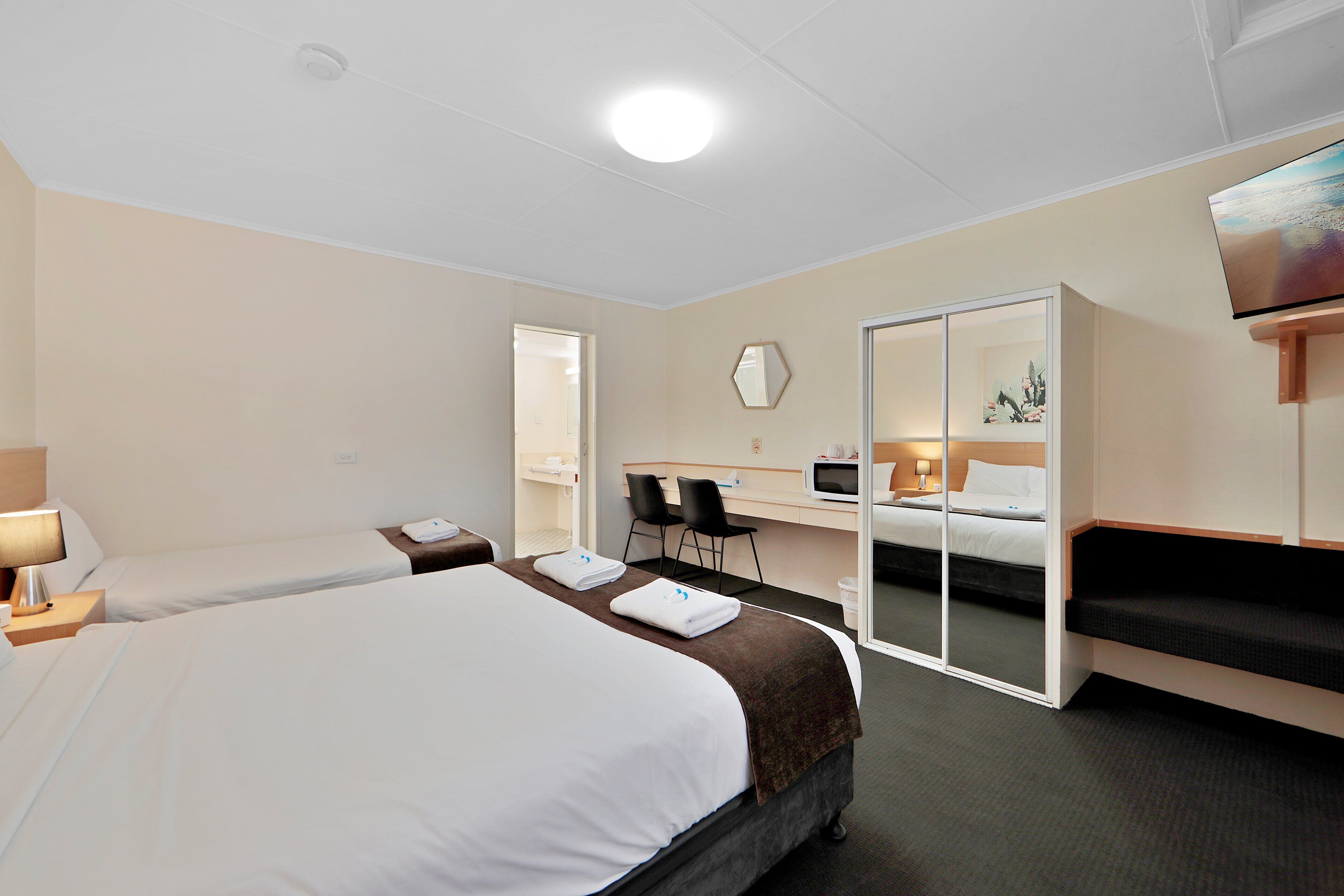 A hotel room with two beds, a desk with a chair, a TV, and a sliding door closet.