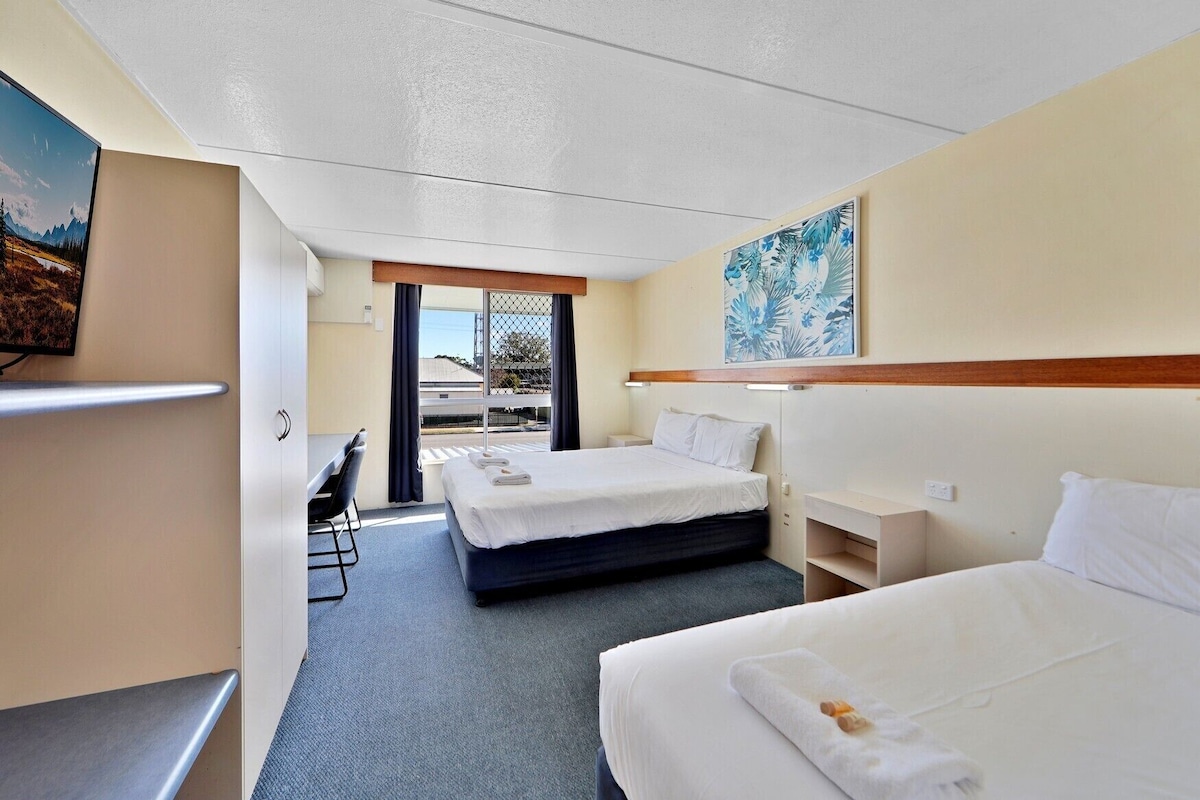 A hotel room with two beds, a desk, and a chair.