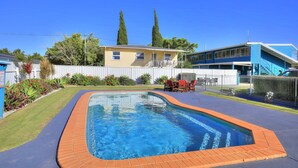 A swimming pool with a brick border, surrounded by a paved area and a fence. - Oscar Motel (Bundaberg West)