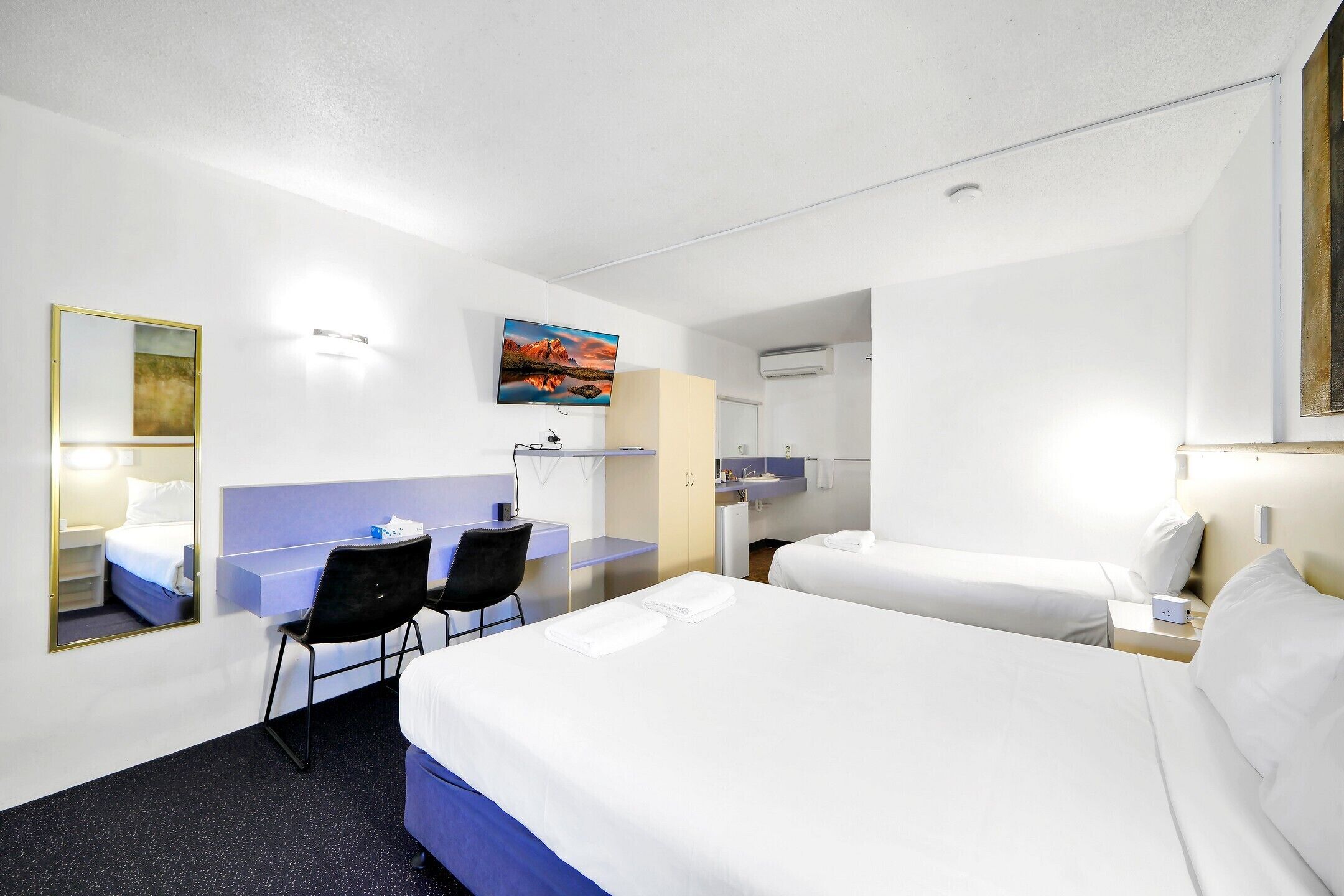 A hotel room with a large bed, a desk with a chair, a small table, and a mirror.