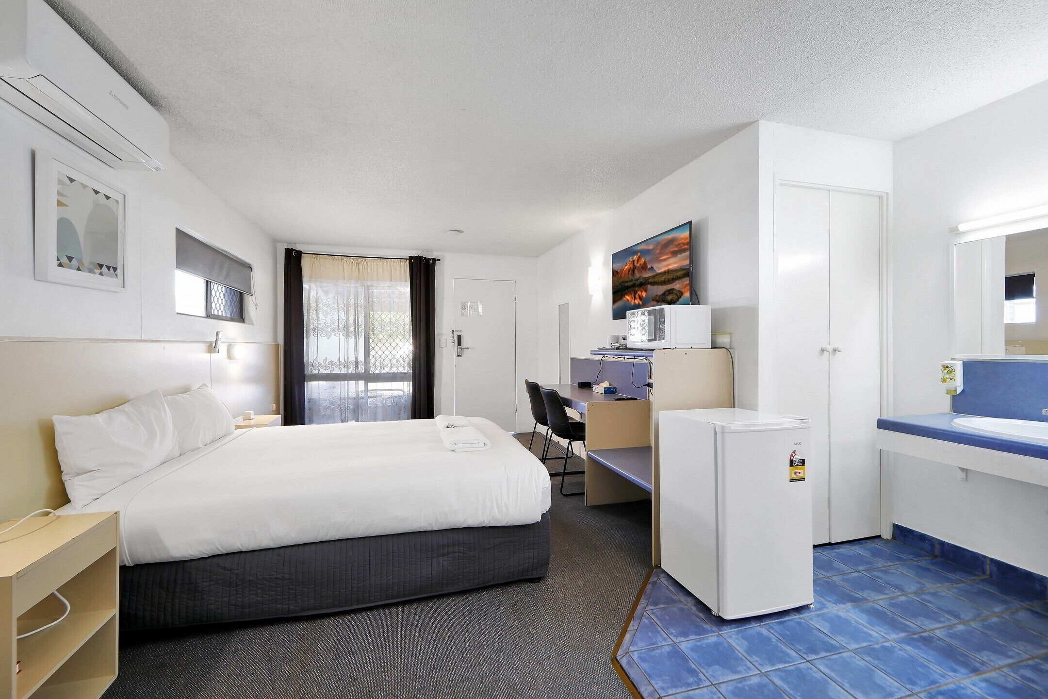A hotel room with a bed, desk, and a small kitchenette.