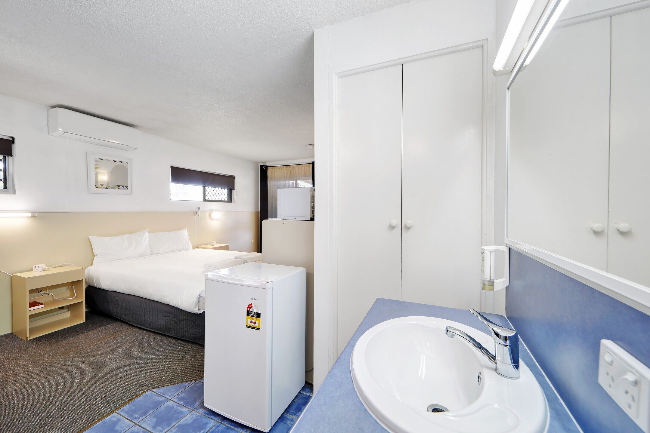 A hotel room with a bed, a small refrigerator, a sink, and a mirror.