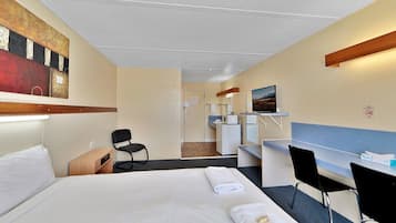 Habitación de hotel con cama, escritorio, silla, televisor y baño visible a través de una puerta abierta.