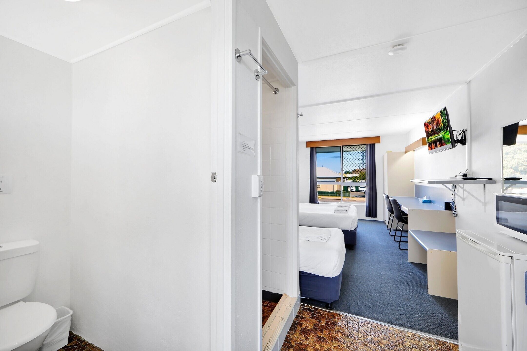 A compact hotel room with a shower, a small kitchenette, a dining area with a table and chairs, and a view through a window.