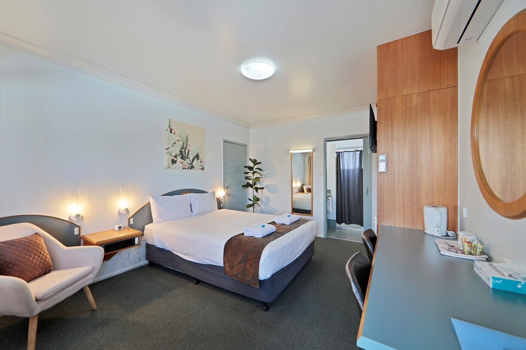 A hotel room with a bed, a desk, a chair, a mirror, and a shower area.
