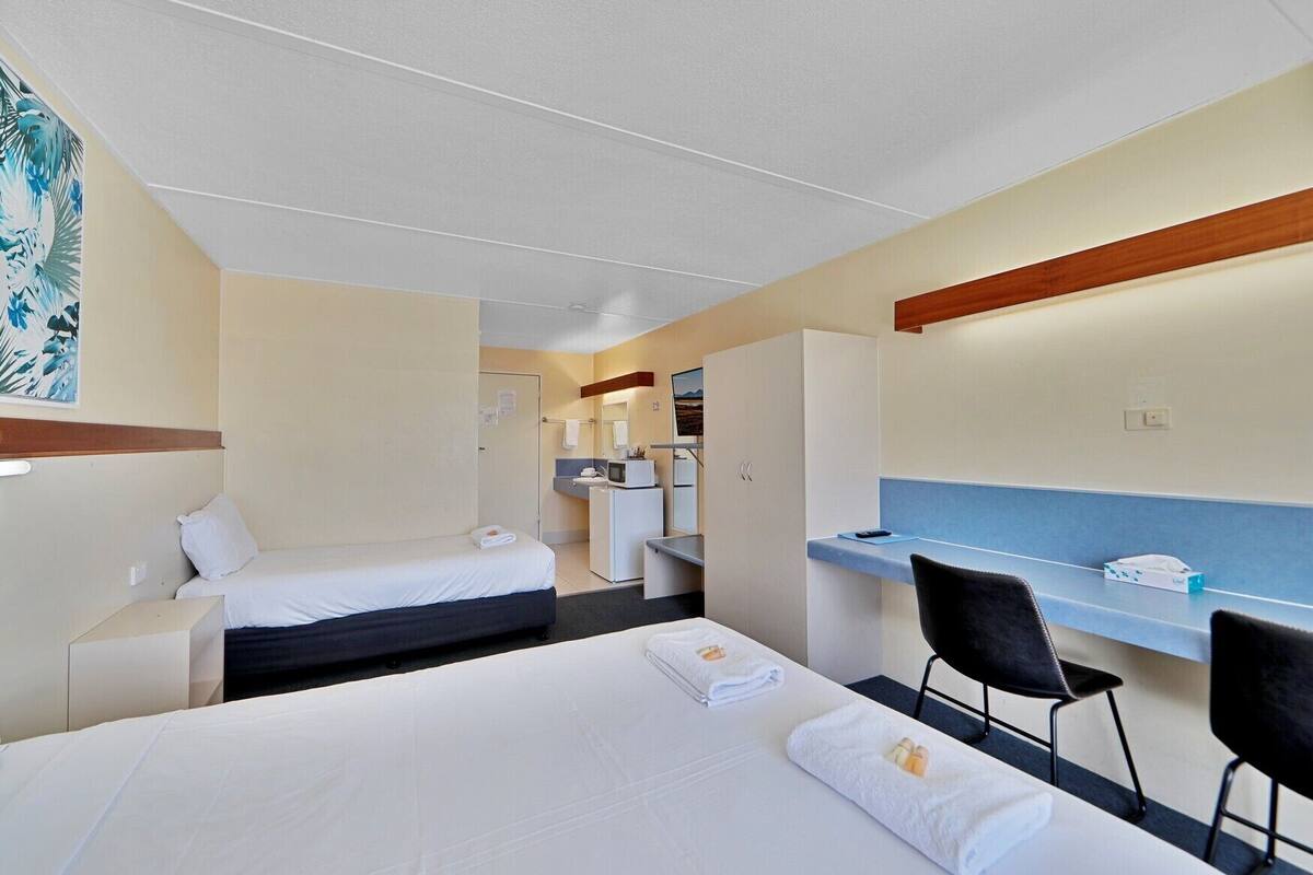 A hotel room with two beds, a desk, a chair, a small kitchenette, and a bathroom.