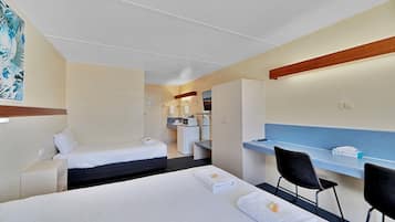 A hotel room with two beds, a desk, a chair, a small kitchenette, and a bathroom.