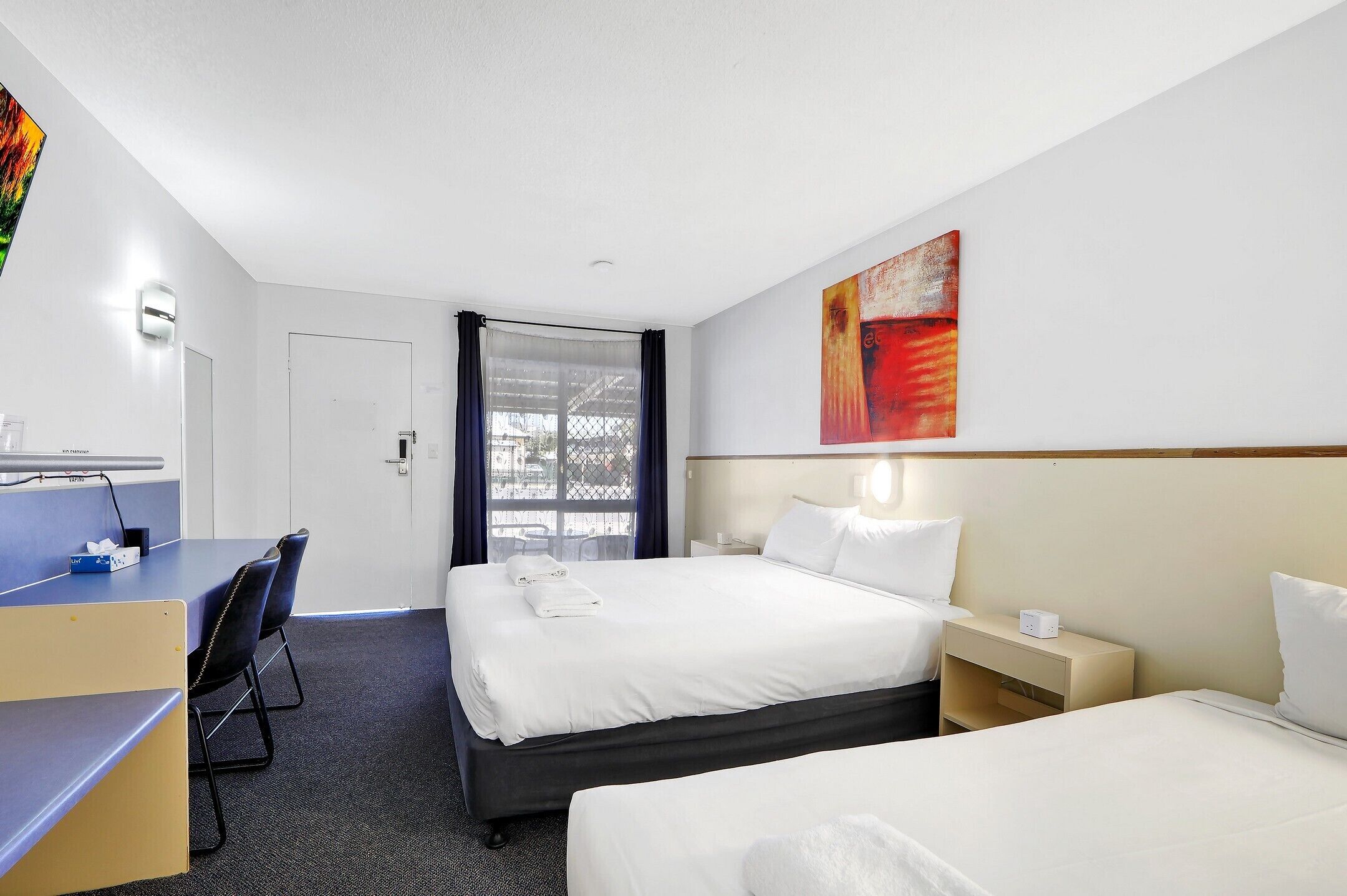 A hotel room with two beds, a desk, and a chair.