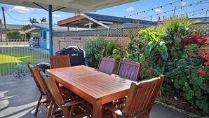 An outdoor patio with a wooden table and chairs, surrounded by plants and flowers. - Oscar Motel (Bundaberg West)