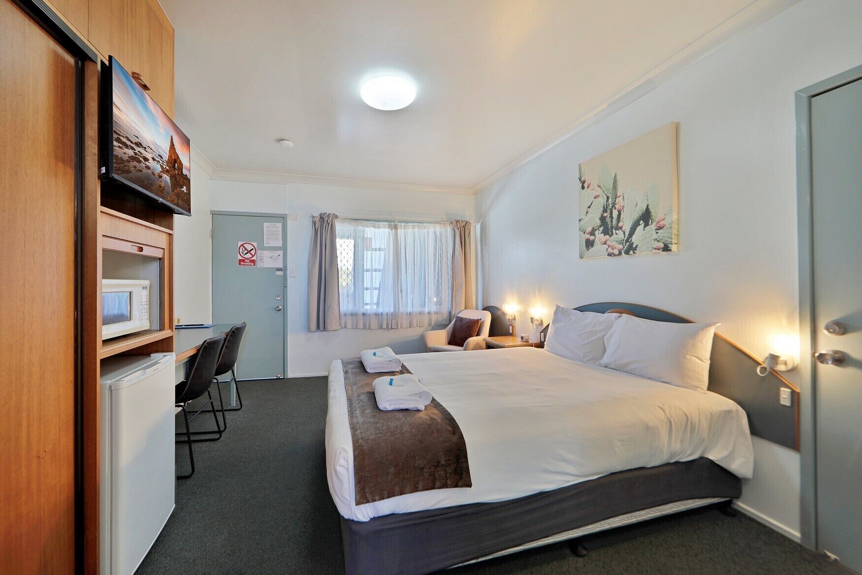 Ein Hotelzimmer mit einem Bett, einem Schreibtisch mit Computer, einer Mikrowelle und einer Tür mit Nichtraucher-Schild.
