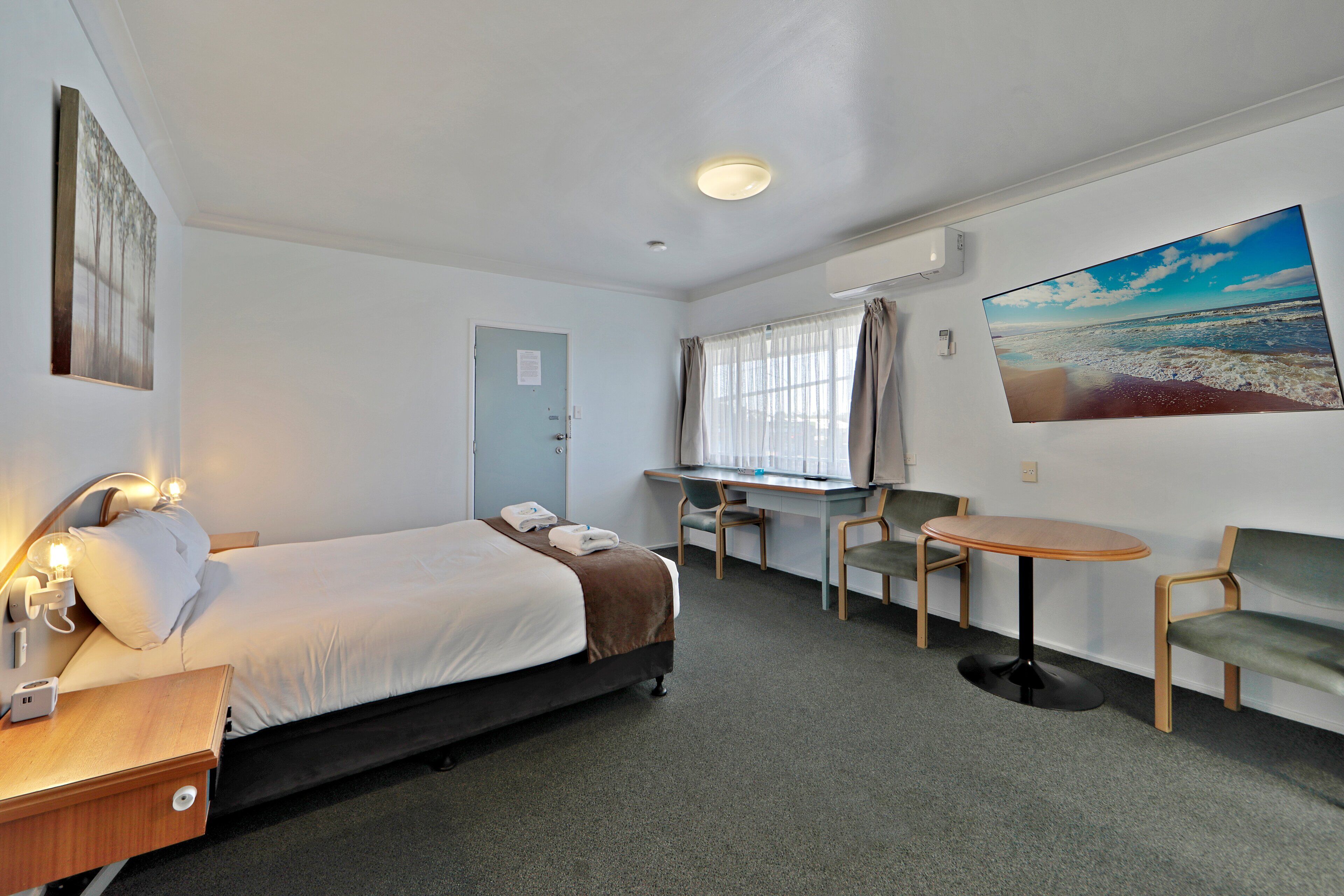 A hotel room with a bed, a desk, a chair, and a small table.