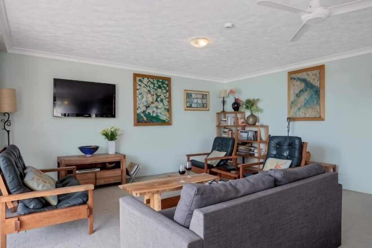 Een woonkamer met een bank, stoelen, een salontafel, een televisie en kunstwerken aan de muur.