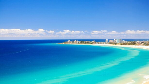 A coastal cityscape with a clear blue sea, sandy beach, and a skyline of buildings. - Carool Apartments (Coolangatta)