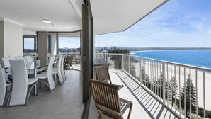 A balcony with a view of the sea, a dining area with chairs and tables, and a modern interior design. - Carool Apartments (Coolangatta)