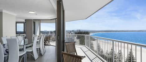 A balcony with a view of the sea, a dining area with chairs and tables, and a modern interior design.