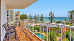 A balcony with two chairs, a pool, and a view of the ocean and buildings. - Carool Apartments (Coolangatta)