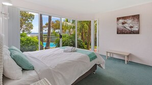 Un dormitorio con una cama grande, un banco y vistas a zonas verdes y una piscina a través de amplios ventanales.