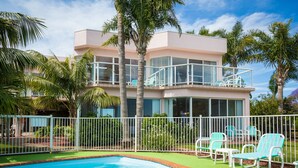 Un edificio moderno de dos pisos con piscina, asientos exteriores y palmeras.