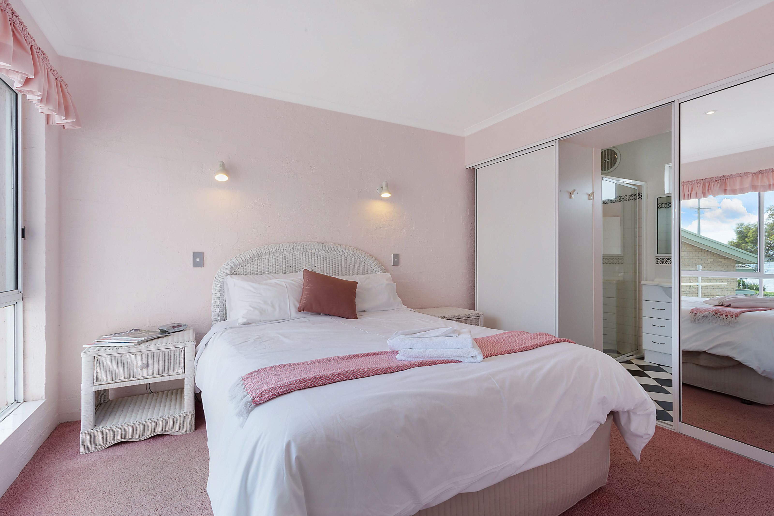 A bedroom with a large bed, a bedside table, a mirror, and a window.