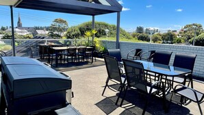 An outdoor patio with tables and chairs, a barbecue grill, and a view of a church spire in the background. - City Heart Motel (Warrnambool)