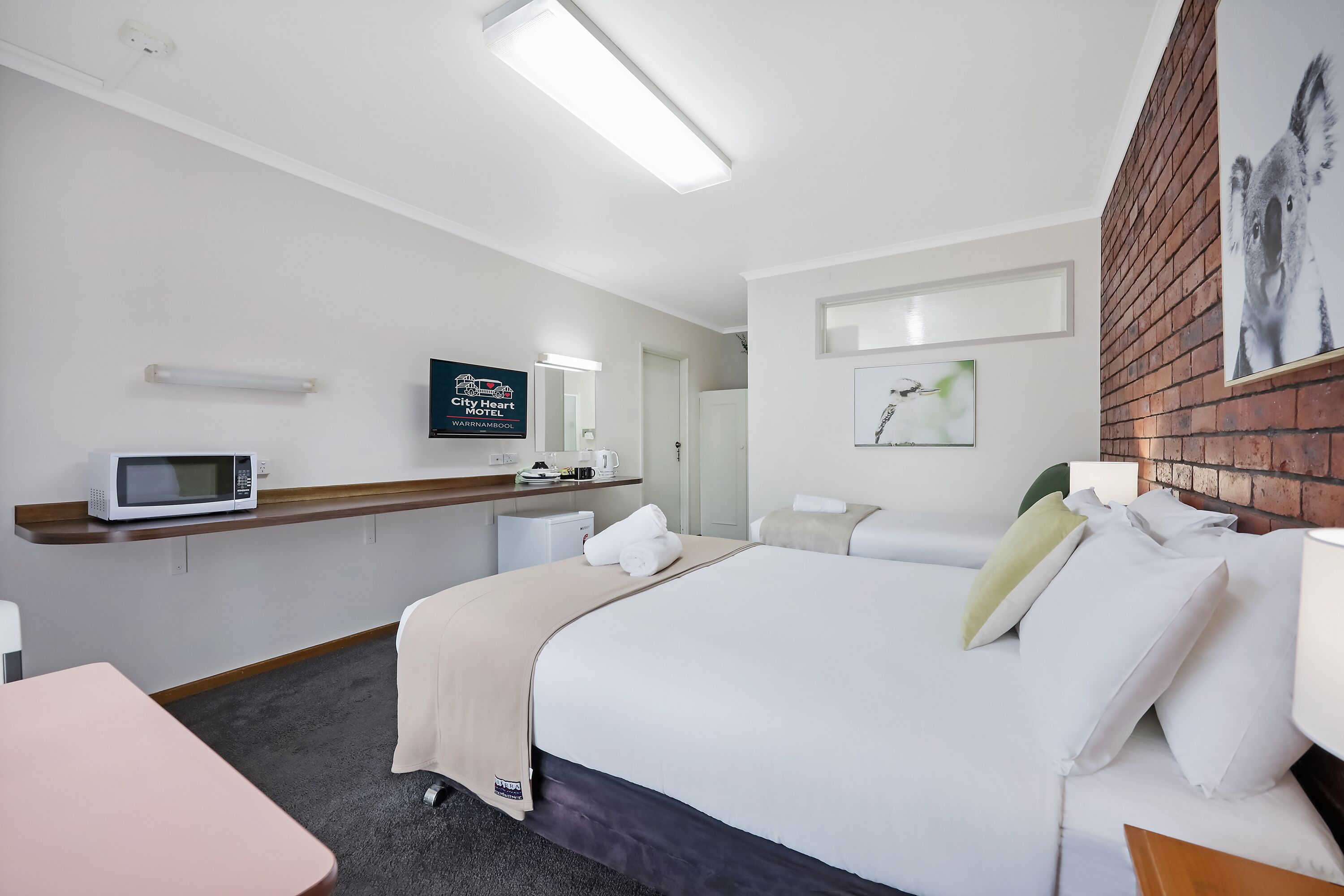 A hotel room with a bed, a desk, a microwave, a television, and a brick wall.
