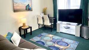 A hotel room with a sofa, a desk with a computer, a television, and a small kitchenette. - City Heart Motel (Warrnambool)