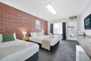 A hotel room with two beds, a brick accent wall, a flat-screen TV, a desk, and a microwave. - City Heart Motel (Warrnambool)