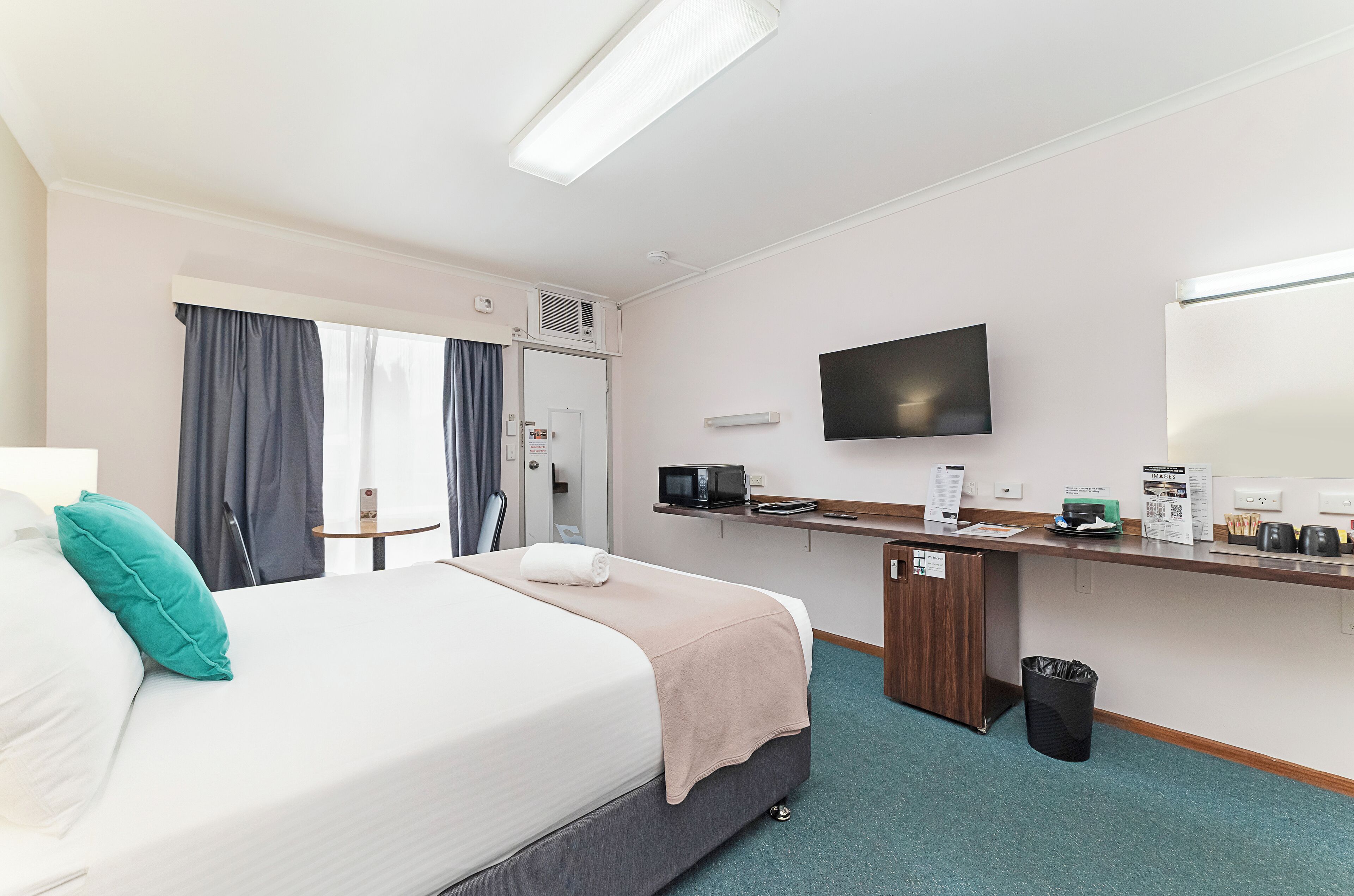 A hotel room with a bed, a desk, a TV, and a trash bin.
