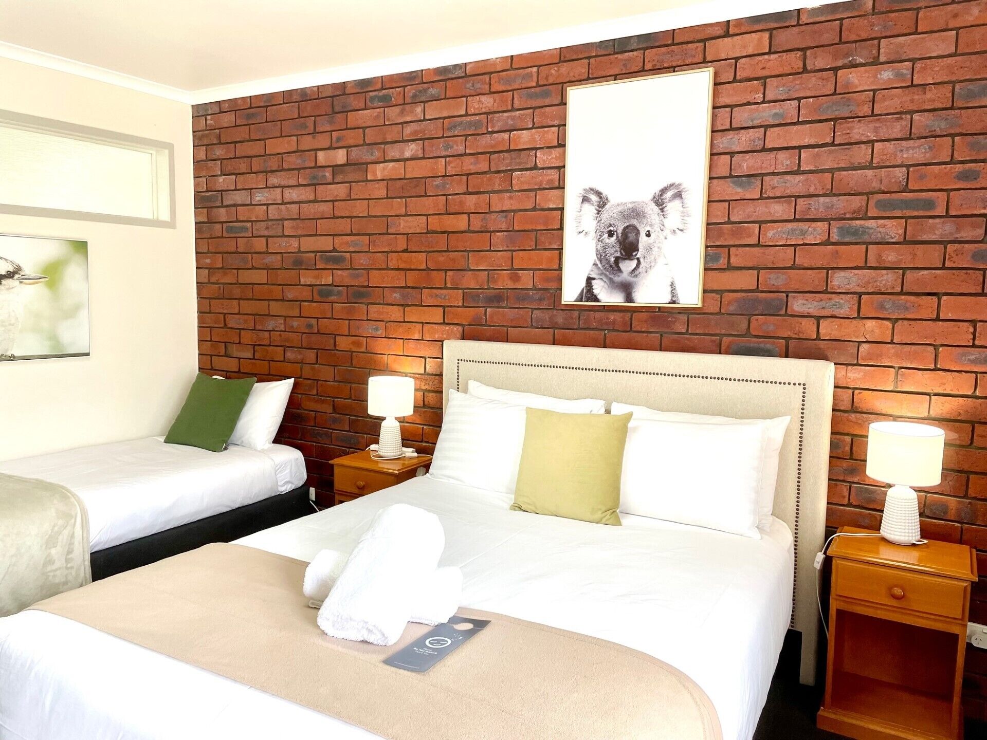 A hotel room with two beds, a brick wall, and a koala picture.