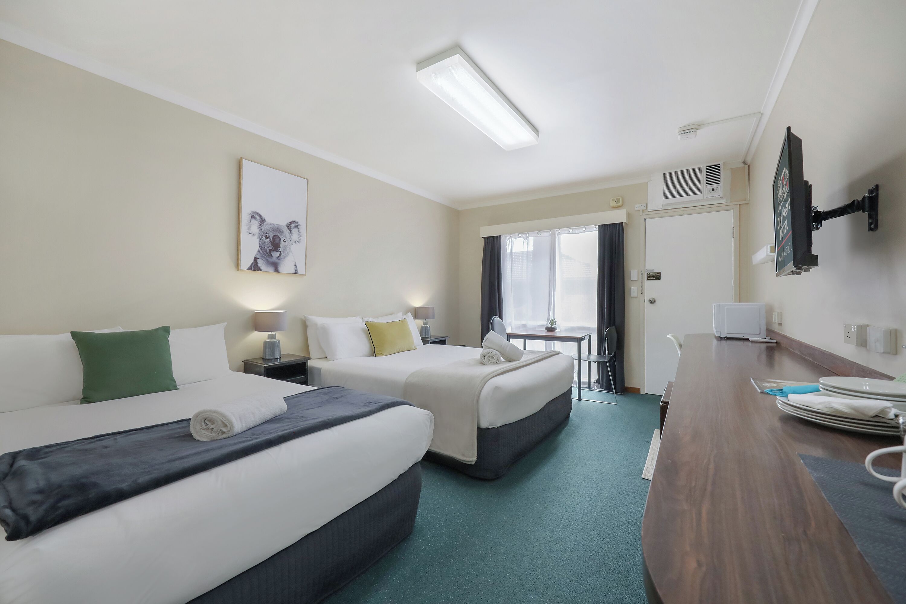 A hotel room with two beds, a desk, a television, and a window with curtains.