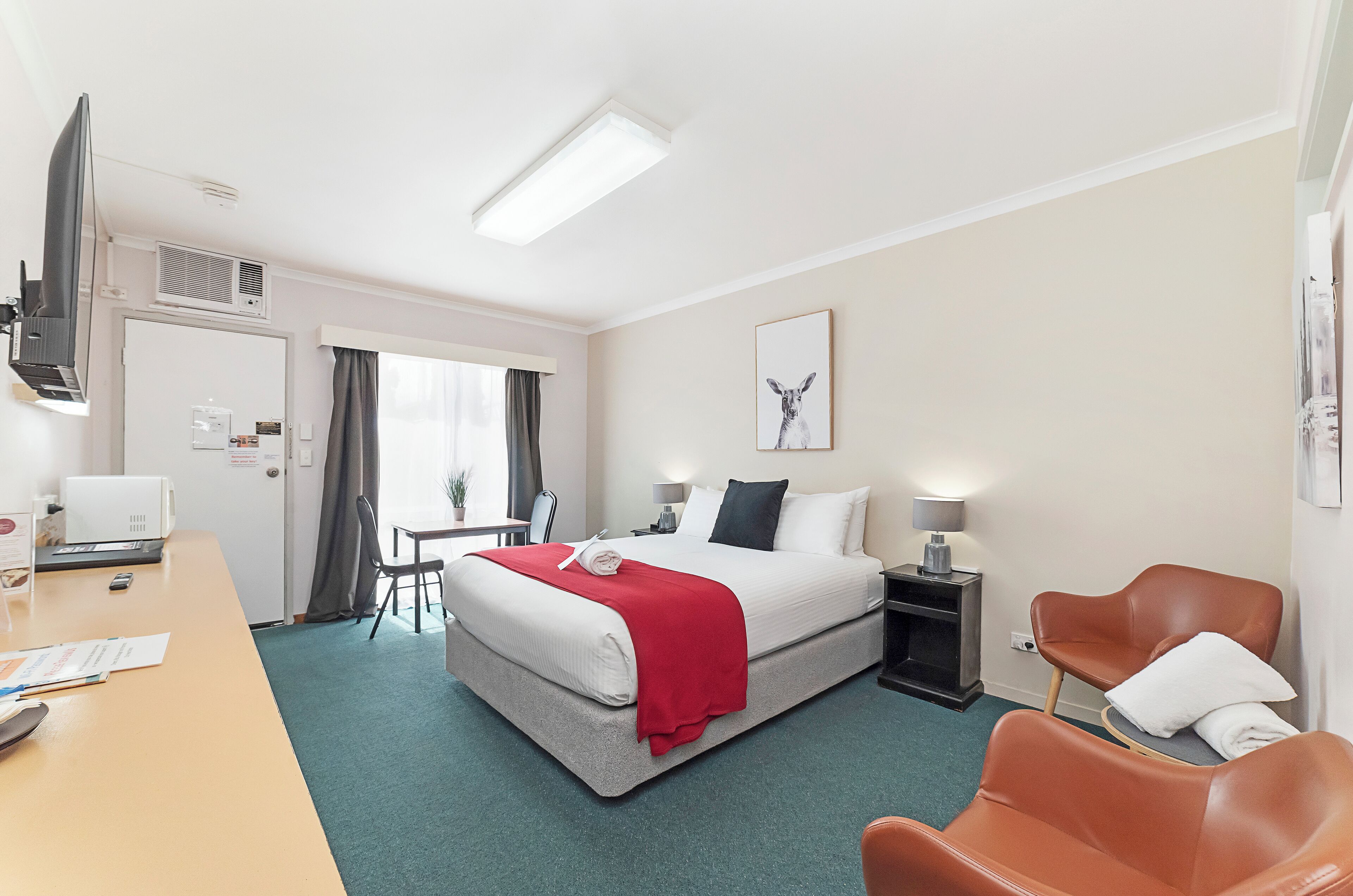 A hotel room with a bed, desk, chairs, and a TV.