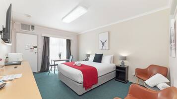 A hotel room with a bed, desk, chairs, and a TV.