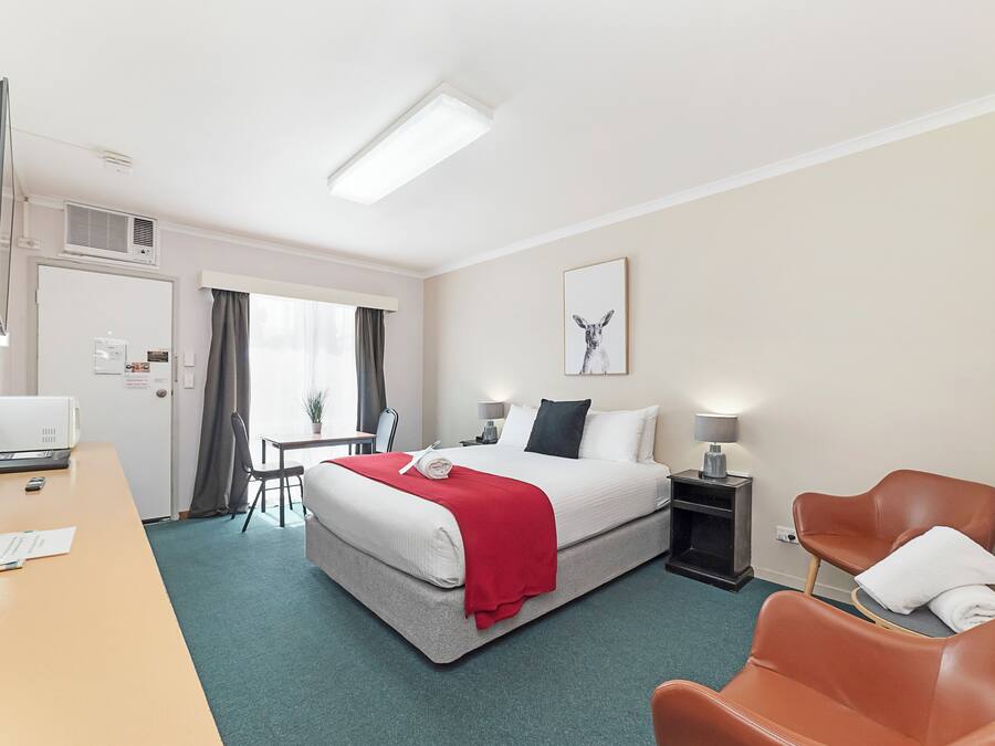 A hotel room with a bed, desk, chairs, and a TV.