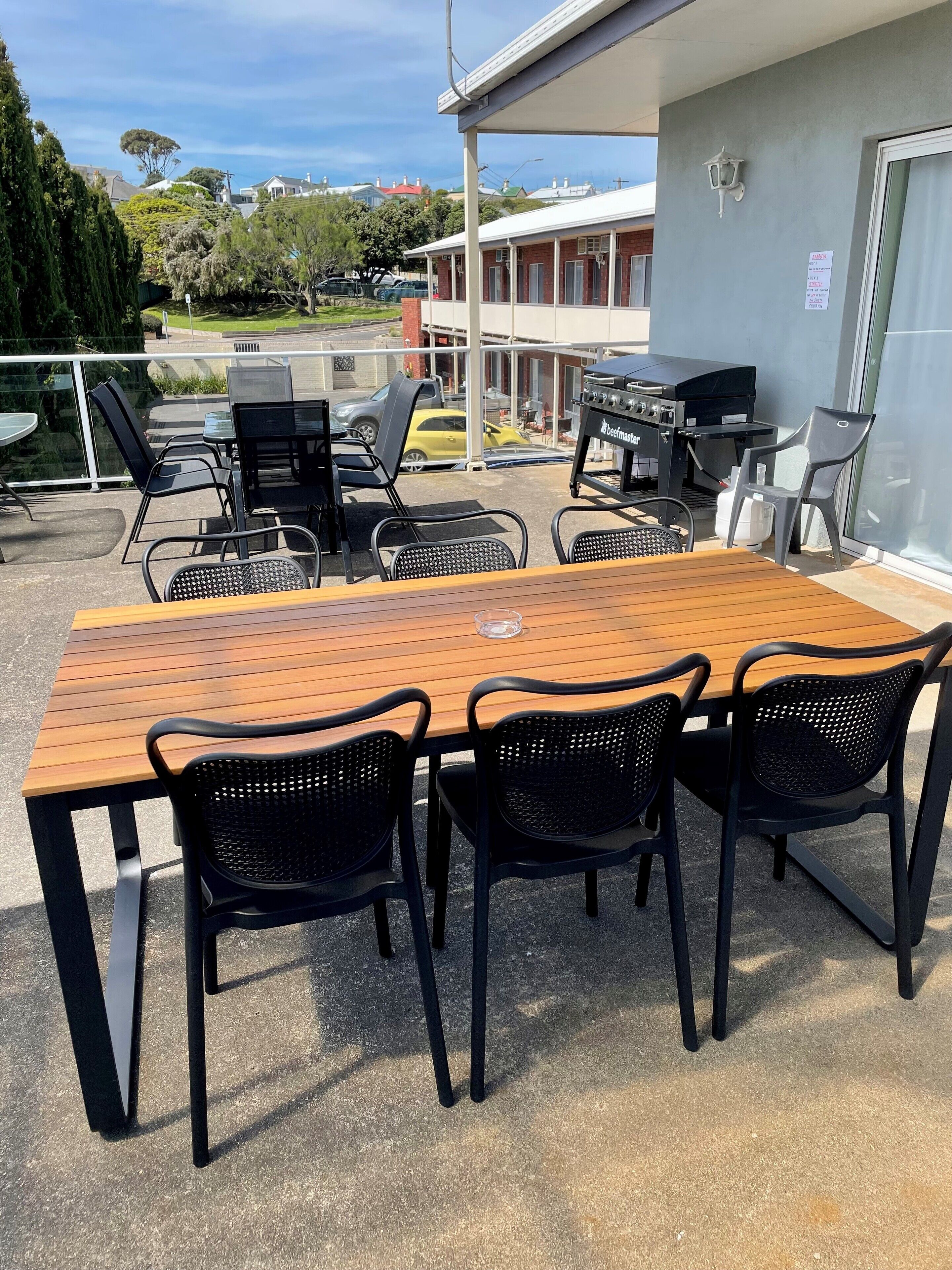 A wooden table with black chairs, a barbecue grill, and a glass door.