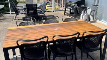 A wooden table with black chairs, a barbecue grill, and a glass door.